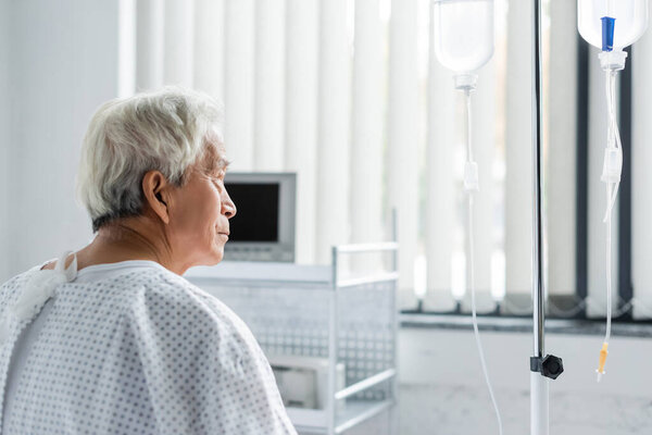 Вид сбоку пожилого азиатского пациента, рассматривающего внутривенную терапию в больнице 