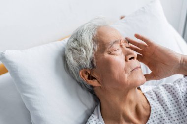 Hasta Asyalı adam hastane koğuşunda yatakta yatıyor. 