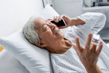 Nabız oksimetresi olan gülümseyen Asyalı hasta klinikte akıllı telefondan konuşuyor. 