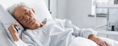 Nabız oksimetresi olan yaşlı Asyalı hasta klinikte yatakta uyuyor. 