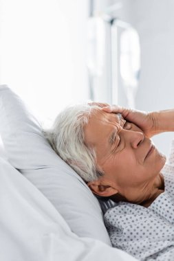 Senior asian patient suffering from headache on bed in clinic  clipart