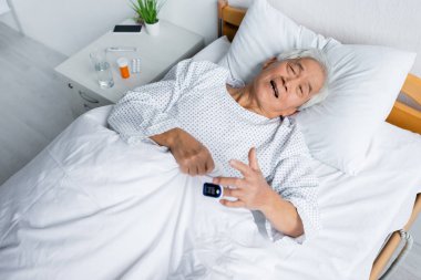 Nabız oksimetresi olan hasta Asyalı bir hastanın klinikteki hapların yanında yattığını yüksek açılı görüyor. 