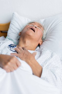 Nabız oksimetresi ve burun kanülü olan Asyalı hasta klinikte yatıyor. 