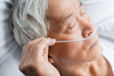 Burun kanülü olan yaşlı Asyalı hasta klinikte gözleri kapalı yatıyordu. 