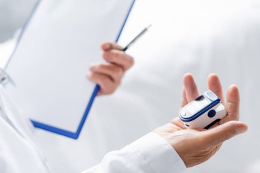 Klinikteki doktorun elinde titreşimli oksitölçer ve bulanık pano var. 