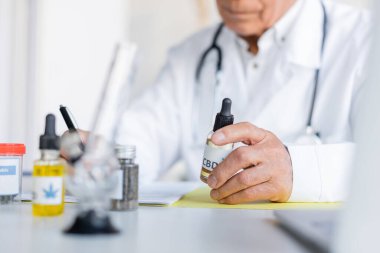 Klinikte esrar ve nargile yanında cbd yağı tutan bulanık bir doktorun görüntüsü. 