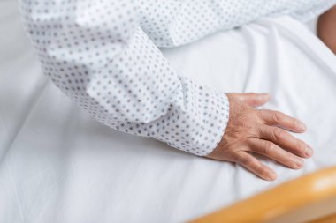 Önlüklü yaşlı bir hastanın klinikteki yatağında oturması. 