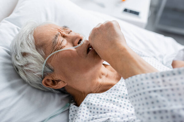 High angle view of senior asian patient with nasal cannula coughing in hospital 