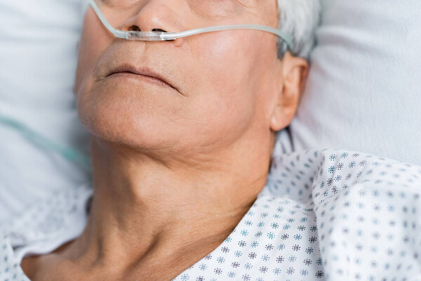 Cropped view of slick patient with nasal cannula lying on bed in hospital 