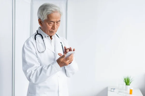 Beyaz Önlüklü Kıdemli Asyalı Doktor Hastanede Akıllı Telefon Kullanıyor — Stok fotoğraf