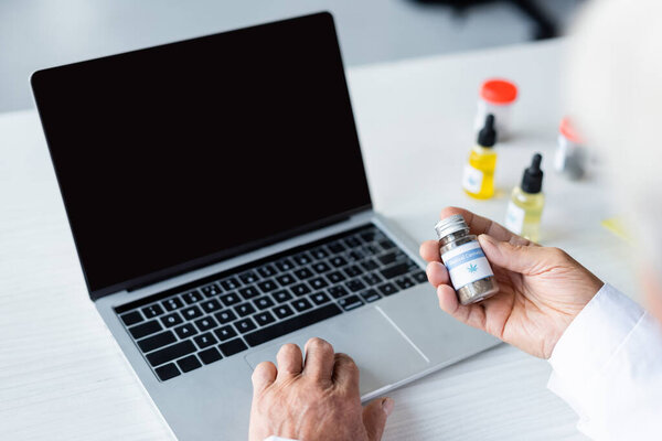 Cropped view of doctor holding medical cannabis near laptop and cbd oil 