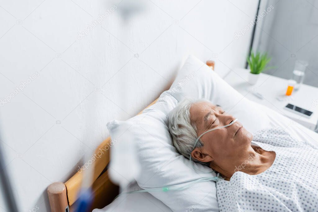 Asian patient with nasal cannula lying on bed in hospital ward 
