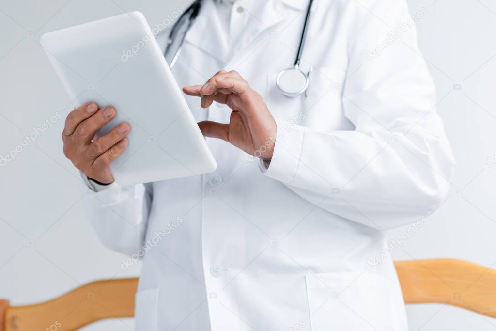 Cropped view of doctor in white coat using digital tablet in clinic 