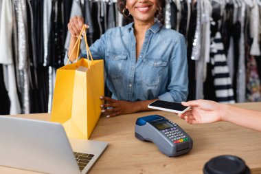 Akıllı telefondan ödeme yapan bir kadının butikte mutlu bir Afro-Amerikan satış elemanı olduğunu gördüm.