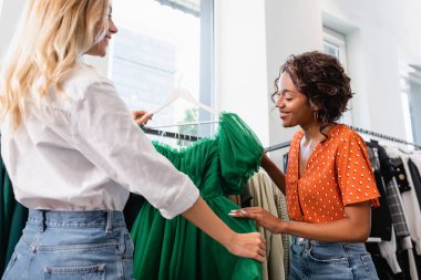 Mutlu çoklu etnik arkadaşlar butikte yeşil elbiseye bakıyor.