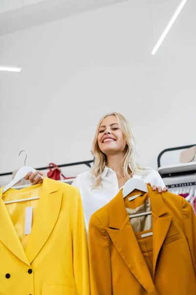 Happy Blonde Woman Holding Hangers Yellow Blazers — Stock Photo, Image