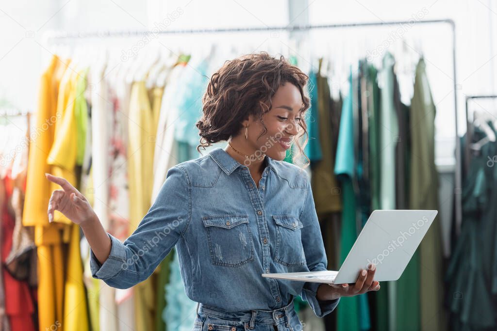 happy african american woman pointing with finger during video call in clothing boutique