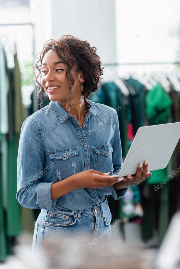 happy african american woman holding laptop in boutique 