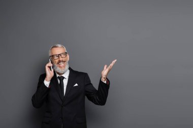 Neşeli orta yaşlı iş adamı cep telefonuyla konuşuyor ve gri renkte işaret ediyor.