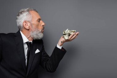 Dövmeli orta yaşlı işadamının kırışık banknotlara üflemesinin yan görünüşü