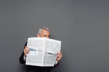 Orta yaşlı işadamı yüzünü gazeteyle kaplıyor.
