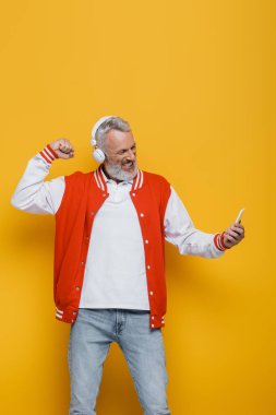 Sarı kulaklıklı mutlu orta yaşlı adam selfie çekerken sarıda sıkılmış yumruğunu gösteriyor. 