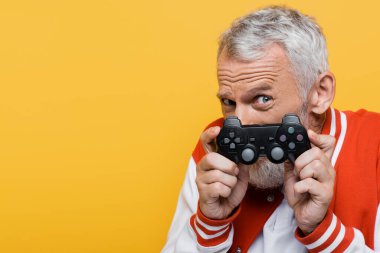 KYIV, UKRAINE - 29 Temmuz 2021: Bombacı ceketli orta yaşlı adam sarıya izole edilmiş joystick ile yüzünü kapatıyor