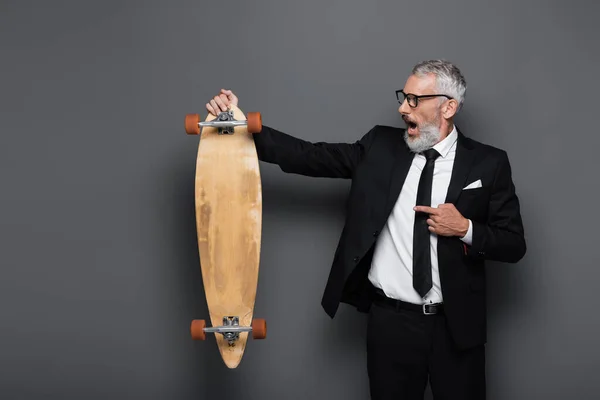 Chockad Och Mogen Affärsman Kostym Och Glasögon Pekar Longboard Grå — Stockfoto