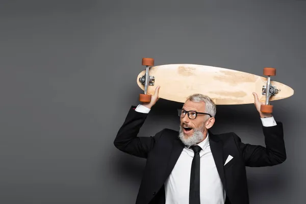Užaslý Zralý Podnikatel Obleku Brýlích Drží Longboard Nad Hlavou Šedé — Stock fotografie