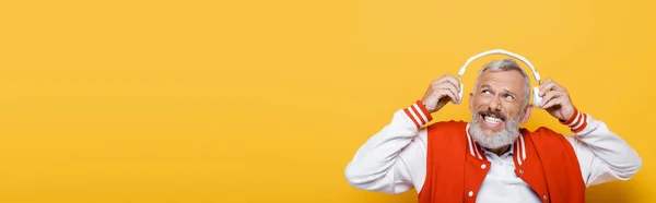 Hombre Mediana Edad Positivo Sosteniendo Auriculares Inalámbricos Aislados Amarillo Bandera — Foto de Stock