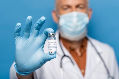 Tıbbi maskeli bulanık doktor elinde Coronavirus aşısı şişesi var.