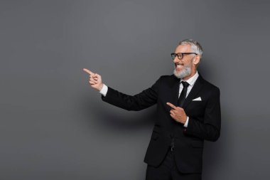 Takım elbiseli neşeli orta yaşlı işadamı ve gri gözlüklü adamı işaret ediyor.