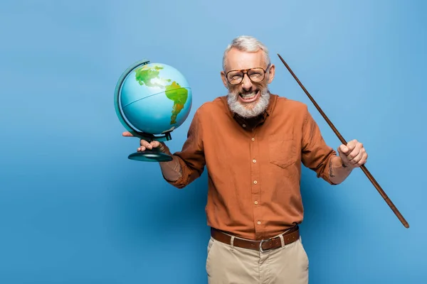 excited middle aged teacher in glasses holding pointer stick and globe on blue