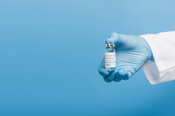 cropped view of doctor in latex glove holding vial with coronavirus vaccine isolated on blue
