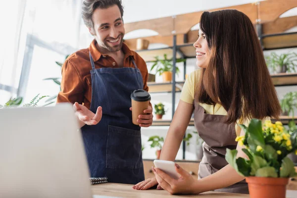 Vendedor Sorrindo Segurando Smartphone Olhando Para Colega Com Café Para — Fotografia de Stock