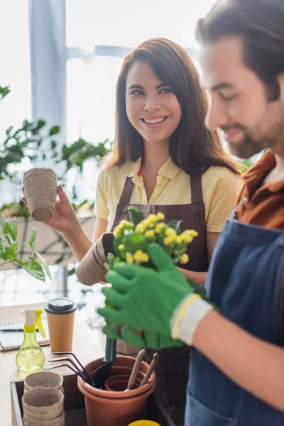 Glimlachende Bloemist Bedrijf Bloempotten Buurt Wazig Collega Tuingereedschap Winkel — Stockfoto