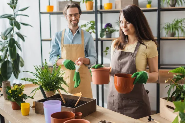 Jovem Florista Segurando Vasos Perto Plantas Colega Sorridente Borrado Loja — Fotografia de Stock