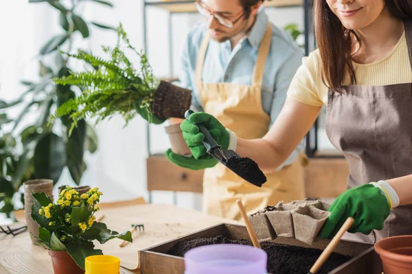 Floristería Sonriente Trabajando Con Tierra Mientras Planta Plantas Cerca Colega — Foto de Stock