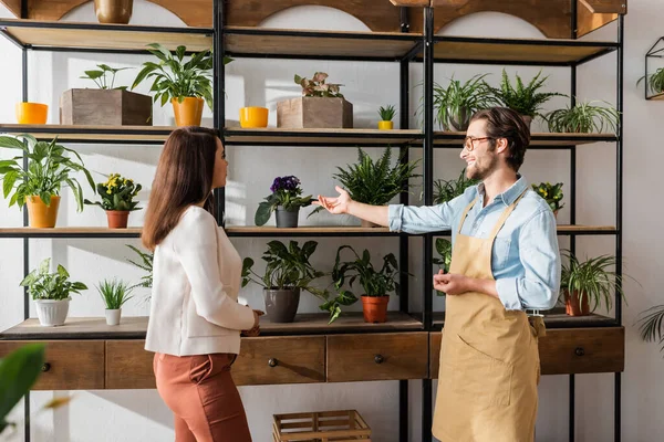 Glimlachende Bloemist Wijst Naar Planten Buurt Van Klant Bloemenwinkel — Stockfoto