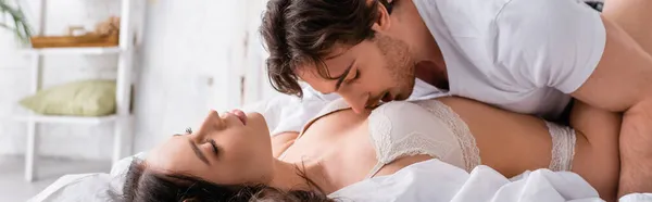 年轻男子吻着穿着胸罩的性感女子 双目紧闭 高举横幅躺在床上 — 图库照片