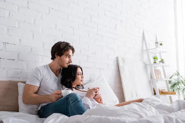 young couple in love sitting on bed with cups of morning coffee