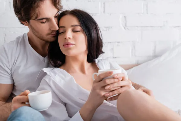 Genç Çift Ellerinde Sabah Kahvesi Tutarken Yatak Odasında Gözleri Kapalı — Stok fotoğraf