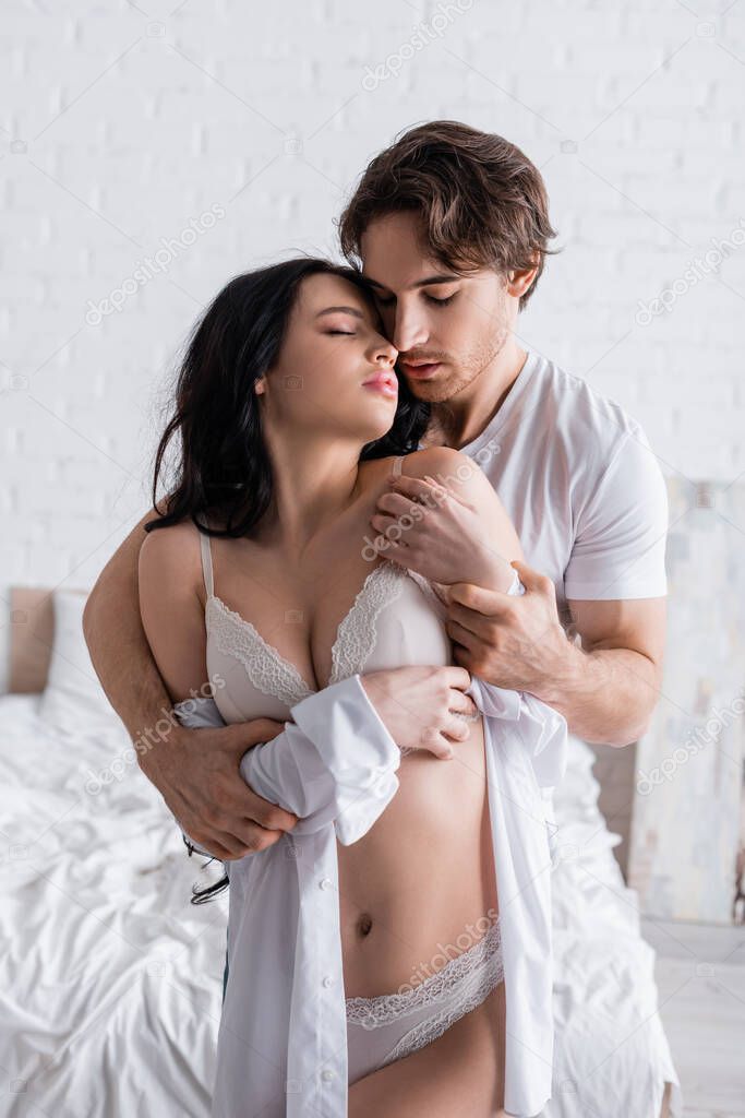 young man embracing passionate woman in underwear and shirt in bedroom