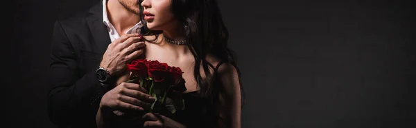 暗い背景に赤いバラを持つ女性の肩に触れる男のクロップドビューバナー — ストック写真