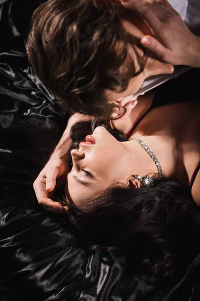宝石の情熱的な女性の近くのぼやけた男のオーバーヘッドビュー目を閉じて黒い寝具に横たわって — ストック写真