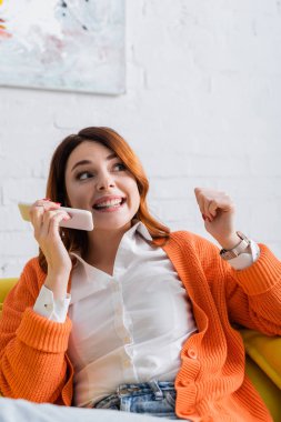 Heyecanlı kadın evde otururken cep telefonundan sesli mesaj yolluyor.