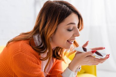 Neşeli kadın evde boş ekranla cep telefonundan sesli mesaj gönderiyor.