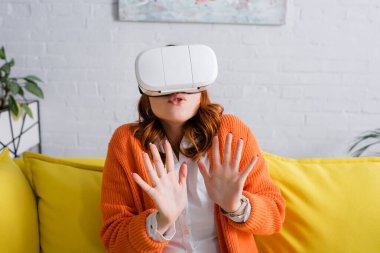 VR kulaklıklı korkmuş kadın evde oynarken jesti durdurduğunu gösteriyor.