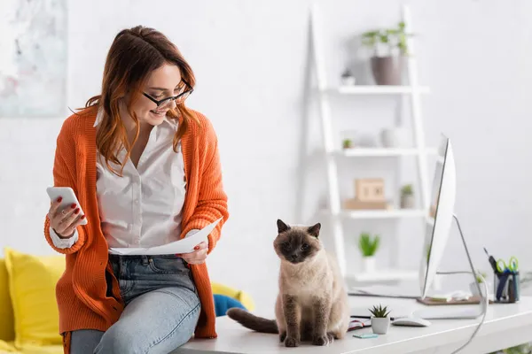 Freelance Souriant Avec Smartphone Documents Regardant Chat Assis Sur Bureau — Photo