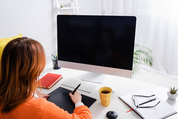 back view of designer working on graphic tablet near computer monitor with blank screen at home
